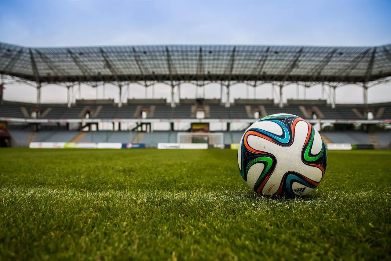 about-us Close-up of a soccer ball on a lush grass field with an empty stadium in the background.